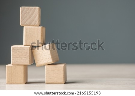 Wooden cubes are built as a tower and risk falling down caused by the only one on the base is in the wrong composition, looking unstable and fragile. Weakest one in a teamwork Royalty-Free Stock Photo #2165155193