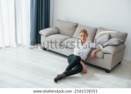 In black jeans. Woman in formal wear sitting on the floor near sofa in domestic room.