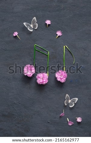 Notes of flowers and stems on a dark stone background with butterflies. Musical summer abstraction top view.