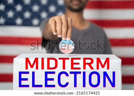 focus on Midterm election, Concept of 2022 American Midterm Elections showing by placing I voted sticker on ballot box with Midterm Election sign in front of US flag