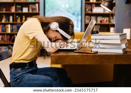 Sleepy tired young female student falling asleep in the university library Royalty-Free Stock Photo #2165175717