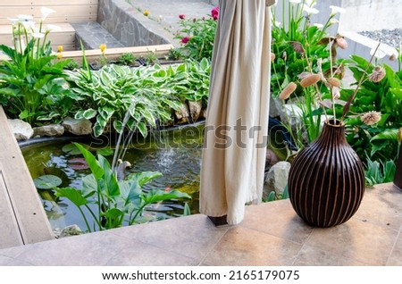 Decorating a small garden artificial pond with goldfish near patio rest area. Plants and stones in the design of the pond