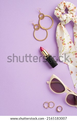 Makeup beauty concept. Top view vertical photo of stylish scarf scrunchy lipstick sunglasses gold earrings and rings on isolated lilac background