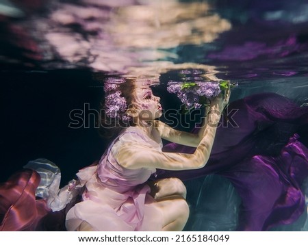 woman with lilac bouquet in colorful clothes on the dark background swimming underwater