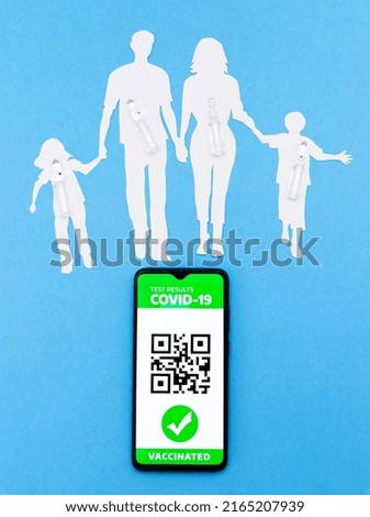 Cellphone with app of digital immunity passport and a silhouette of a family cut out of paper with ampoules on a blue background. The concept of vaccination. Flat lay. Vertical
