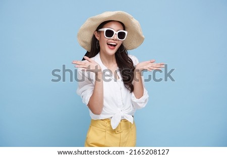 Happy beautiful Asian woman dressed in summer clothes smiling with open hand gesture of welcome isolated on blue background.
