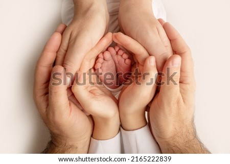 The palms of the father, the mother are holding the foot of the newborn baby. Feet of the newborn on the palms of the parents. Studio photography of a child's toes, heels and feet. Concept. Royalty-Free Stock Photo #2165222839