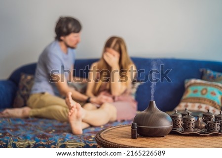 Man comforting his upset partner at home in living room. Aromatherapy Concept. Wooden Electric Ultrasonic Essential Oil Aroma Diffuser and Humidifier. Ultrasonic aroma diffuser for home. Woman resting Royalty-Free Stock Photo #2165226589