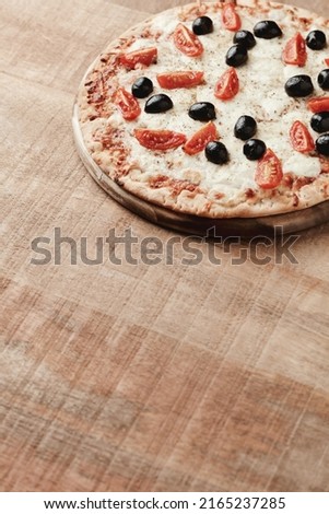 Pizza with mozzarella cheese, cherry tomatoes, black olives and oregano. Home made food. Concept for a tasty and hearty meal. Wooden background. Copy space. 