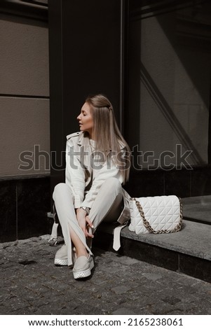 portrait of beautiful blonde girl dressed in beige leather jacket tank top, sweater, leggings flares with slits, loafers, accessories, bag, stylish trendy fashion outlook, lifestyle model sitting