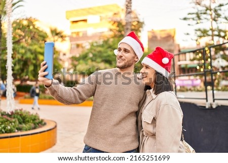 Man and woman couple wearing christmas hat make selfie by the touchpad at park