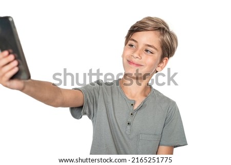 Portrait of smiling young boy holds mobile phone in front of himself and takes a selfie isolated