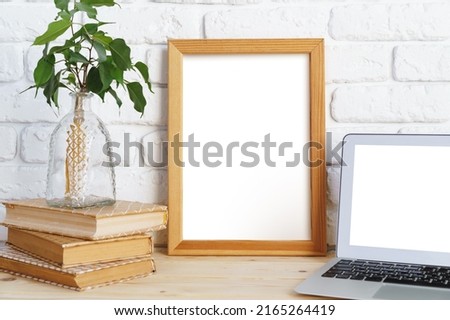 Blank picture frame on wooden table with books and laptop, copy space