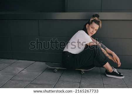 Young beautiful woman with braids and tattoos wearing casual clothes standing with skateboard on city street.