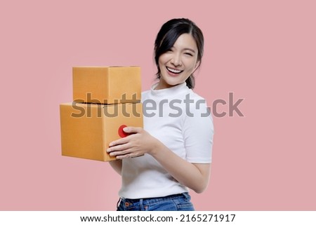 Happy Asian woman holding package parcel boxs isolated on pink screen background. Delivery courier and shipping service concept.