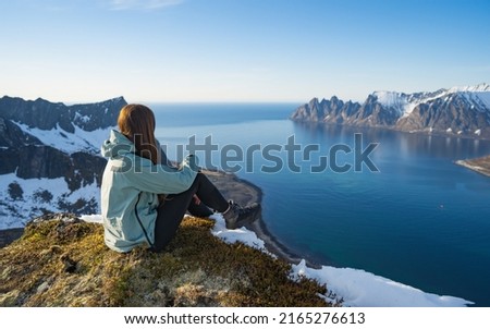 Rear view of hiker woman on top of mountain peak in rocks sitting in silence. Best Norway hike. Amazing nature view. Adventure lifestyle outdoor activity Senja islands. Artistic picture. Beauty world