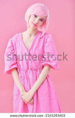 Portrait of a cute teen girl with bright pink makeup and pink hair posing in fashionable pink dress. Pink background. Beauty, fashion. 