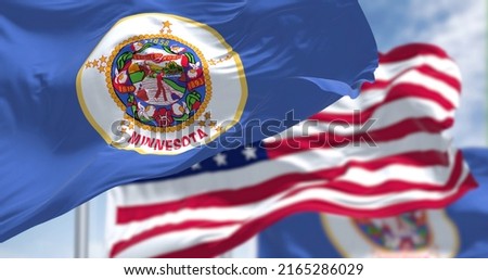The Minnesota state flag waving along with the national flag of the United States of America. In the background there is a clear sky. Minnesota is a state in the upper Midwestern United States