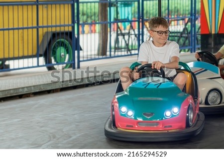 Portrait of teenage boy in glasses driving an electric car in amusement park. Child on Bumper car Royalty-Free Stock Photo #2165294529