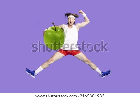 Overjoyed  guy jumping high hold giant apple have snack before training warming up stretching over purple background