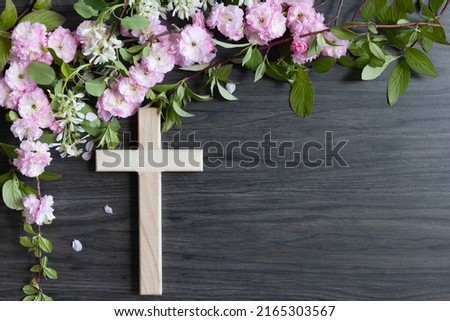 Wood Christian cross and border of branches with spring flower blossoms on a dark wood background with copy space