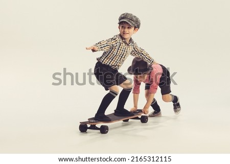 Portrait of playful little boys, children in retro checkered shirts playing together, skateboarding, having fun isolated over grey background. Concept of childhood, friendship, fun, lifestyle, fashion Royalty-Free Stock Photo #2165312115