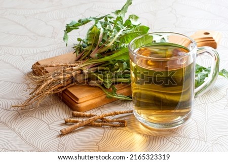 Dandelion herbal tea in mug, dandelion leaves and roots on cutting board. Medicinal plant dandelion  (Taraxacum officinale) is used in herbal medicine and healthy nutrition Royalty-Free Stock Photo #2165323319