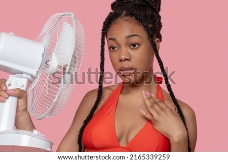 Young african american woman holding a fan looking tired from heat