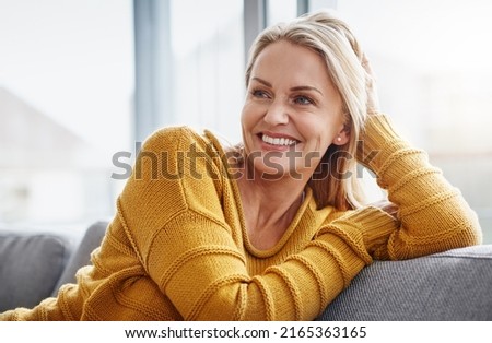 Relaxing really lifts the spirits. Shot of an attractive mature woman relaxing on the sofa at home. Royalty-Free Stock Photo #2165363165