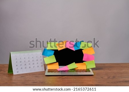 Laptop with colorful sticker notes and calendar on wooden desk. Notebook pc with open black screen in the office.