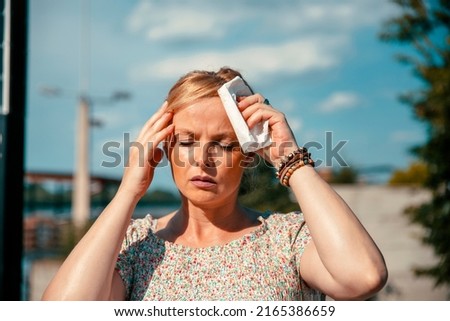 Woman feeling bad pain, heat, woman with heatstroke. Having sunstroke at summer hot weather. Mature Female under sunshine suffering from Headache. Person holds paper tissue on head Royalty-Free Stock Photo #2165386659