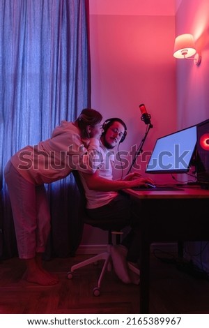 Young couple in room with neon light are using modern personal computer at home