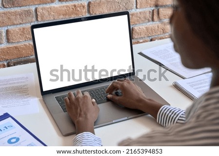 Young black African business woman using laptop computer device white blank empty mockup template screen digital technology working online, typing sitting at desk at home office. Over shoulder view Royalty-Free Stock Photo #2165394853