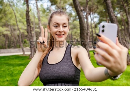 Young brunette girl smiling happy wearing sportive clothes on city park, outdoors smiling with happy face while taking selfie doing victory sign or gesture, showing peace. Number two.