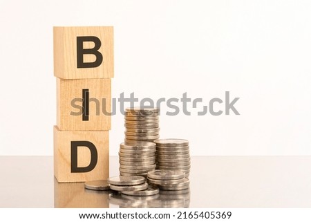 the letters bid is laid out of wooden cubes with letters on white background with coins