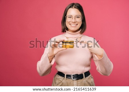 Photo of cheerful young student woman pointing at her new credit card over pink background
