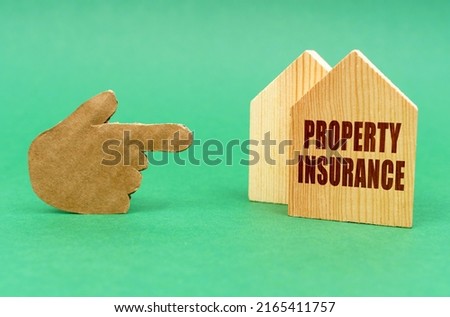 Business real estate concept. On a green surface, a hand points to a house with an inscription - Property insurance