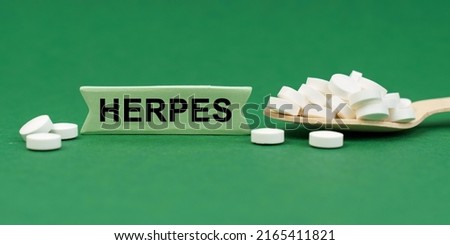 Medicine concept. On a green surface, a wooden spoon with pills and a sign with the inscription - HERPES
