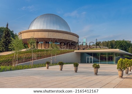 Modern entrance to the Silesian planetarium after renovation. Aluminum panels on the dome of the planetarium shining in the light of the setting sun. Observation tower in the background. Royalty-Free Stock Photo #2165412167