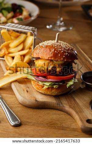 Big cheeseburger with french fries isolated on white background. Hamburger with beef patty onion, tomato, lettuce pickles, melted cheddar, mustards, tomato jam, mayo.