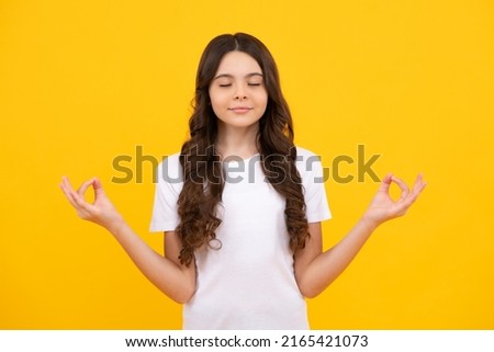 Little teenager kid girl 12-14 years old in white shirt hold hands in yoga om aum gesture relax meditate try calm, isolated on yellow background. Royalty-Free Stock Photo #2165421073