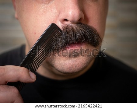 Closeup of a young man brushing his thick black bushy mustache  Royalty-Free Stock Photo #2165422421