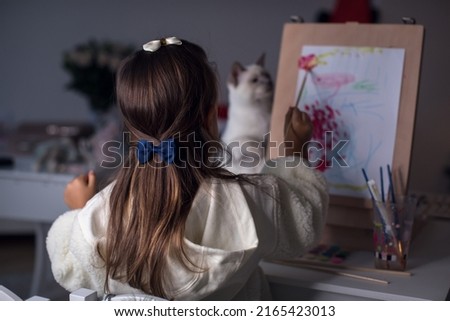 Girl with cat drawing pictures with colored chalks on easel at home. Family spend weekend leisure enjoy favourite common hobby.