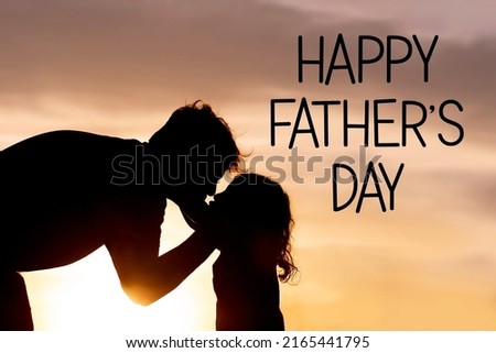 A silhouette of a loving father kissing and hugging his young toddler child at Sunset on a summer day.