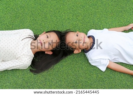Portrait of Asian little boy and girl kid lying on green grass background together.