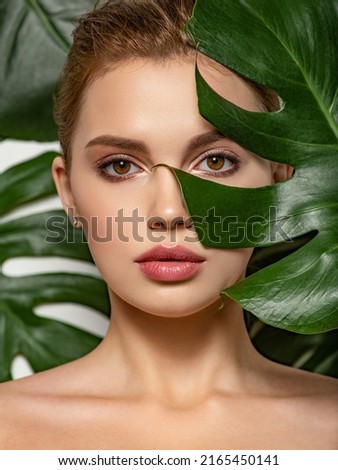 Closeup face of young beautiful woman with a healthy clean skin. Beautiful white girl with big green leaves. Beauty and spa treatment concept. Pretty woman with natural makeup and plant near face Royalty-Free Stock Photo #2165450141