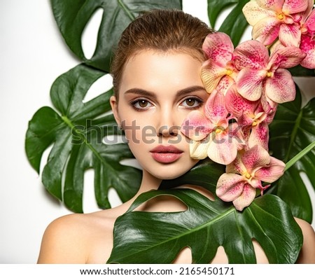 Pretty girl in Skin care beauty treatments concept. 
 Beautiful woman with green leave near face and body. Closeup girl's face with green leave. Model with pink tropical orchid near face.  Royalty-Free Stock Photo #2165450171