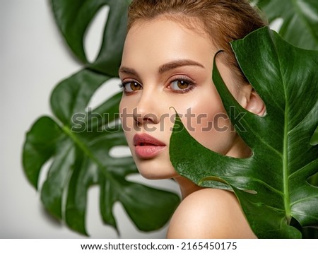Closeup face of young beautiful woman with a healthy clean skin. Beautiful white girl with big green leaves. Beauty and spa treatment concept. Pretty woman with natural makeup and plant near face Royalty-Free Stock Photo #2165450175