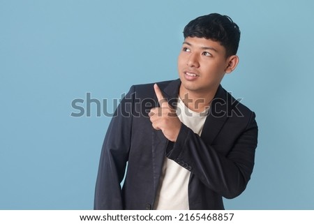 Portrait of young business man in casual suit showing product, pointing at something with finger. Isolated image on blue background