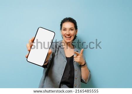 Happy young woman with smartphone on background of blue wall. Blank screen mobile phone for graphic montage.